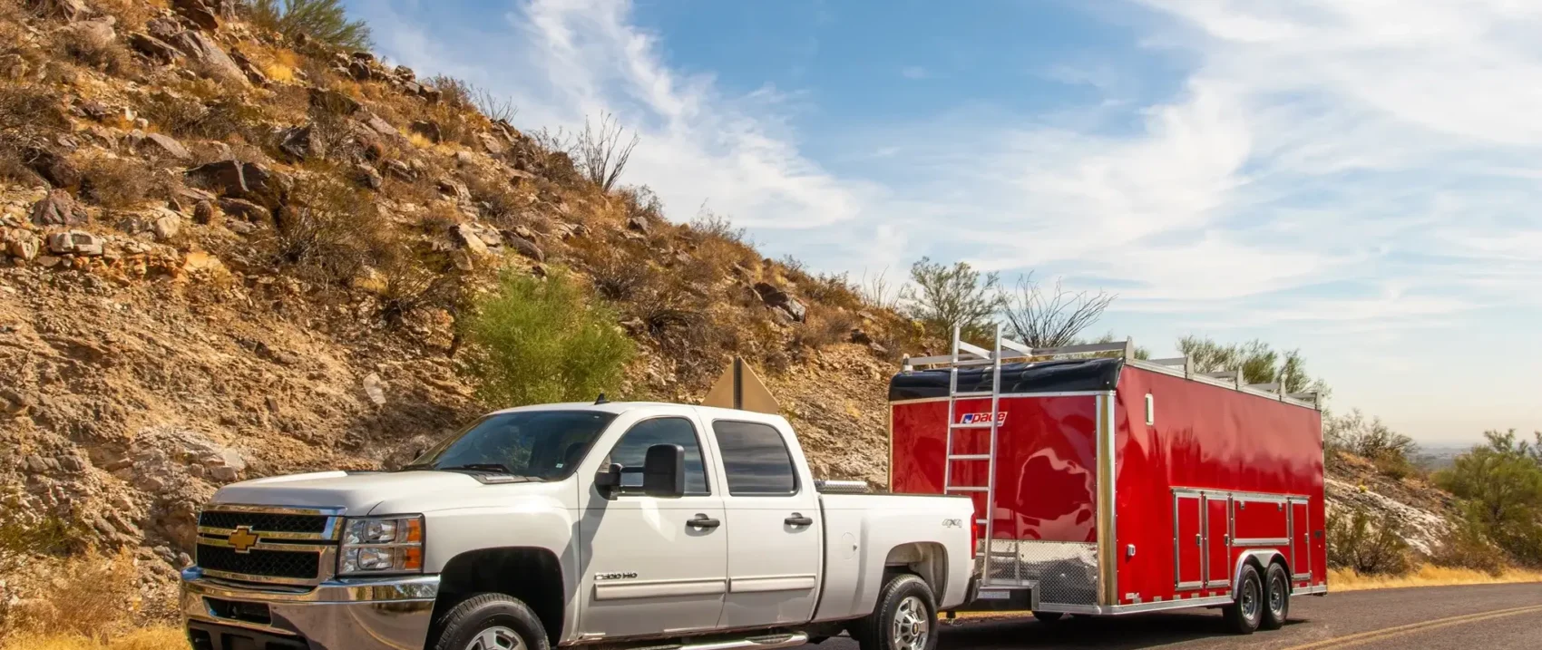 Pickup towing a red trailer on a desert road.